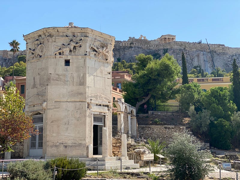 A marble building “The Bathhouse of the winds” with a distant hill “The Acropolis” in the background